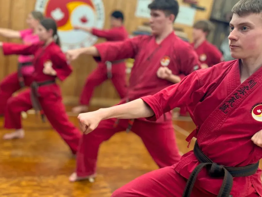 Karate students in red gis practising a front stance punch in class