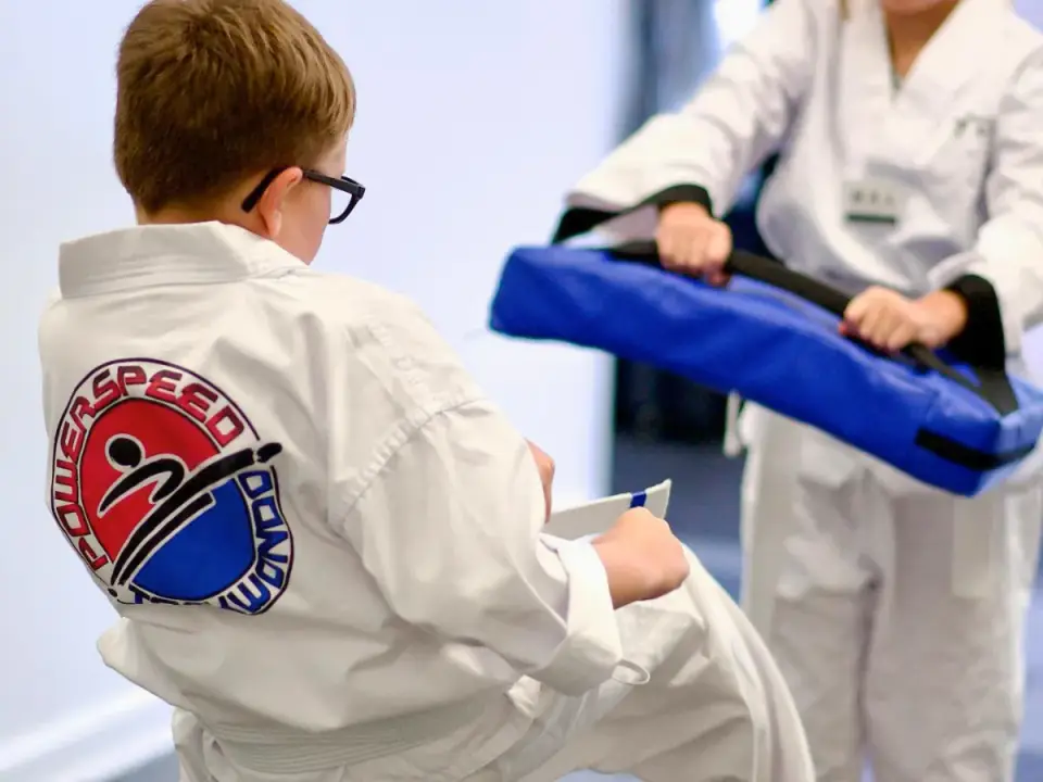 A young student in a white uniform kicking a pad held by an instructor