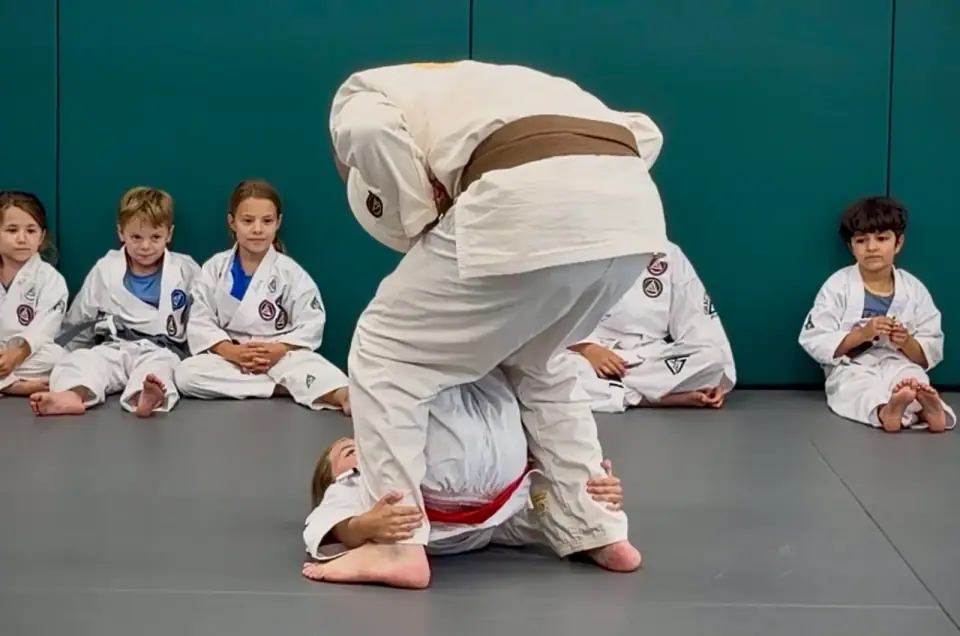 A row of kids in white gis sitting attentively while an instructor demonstrates at Gracie Jiu Jitsu St. Nicolas