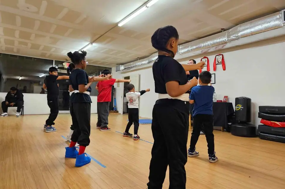 Kids and adults training forms together on the wooden floor at River City Kung Fu